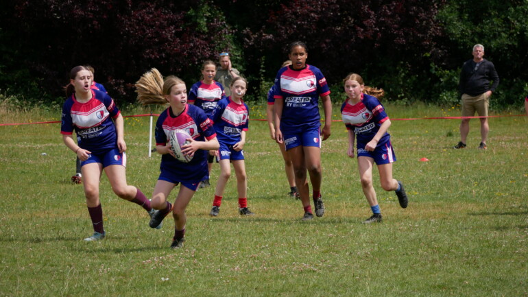 Under 14 players in the middle of a game, one girl carrying the ball